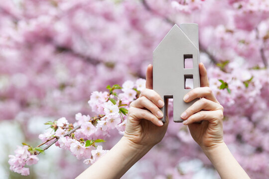 Miniature of the house in the hands against the background of flowers. Housing for refugees and migrants.