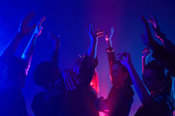 Minimal shot of diverse crowd dancing in club with hands up lit by neon lights