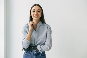 Horizontal portrait of female in jeans and striped shirt with round earrings and smooth long hair posing against white wall with copy space for your advertising content, having bionic prosthetic hand