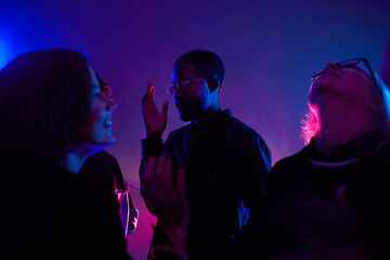 Back lit portrait of black young man dancing in crowd while partying in smoky club lit by neon, copy space