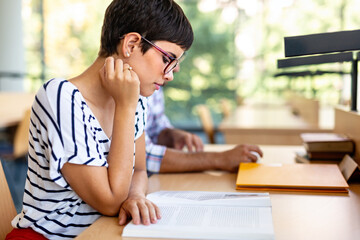 Exhausted young female studying and preparing for exam in college library. Education people concept