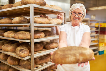 Ältere Frau als Bäckerin zeigt stolz ein frisches Biobrot