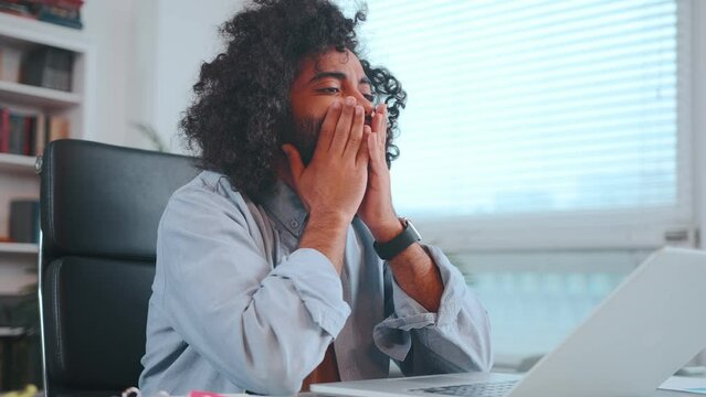 Young worried Arabian man nervous waiting for letter in laptop rubbing face and looking at computer screen does not dare to do something sits at desk in home office. Education, career, technology
