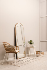 Beautiful mirror, armchair and plant near white wall indoors. Interior design