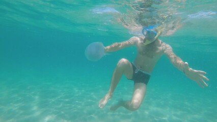 Selfie view of a caucasian man in flippers and a mask swims in the sea next to a jellyfish on a sunny day