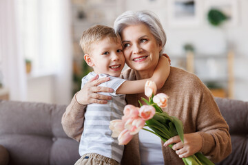 Cheerful little boy giving flowers to grandmother - obrazy, fototapety, plakaty