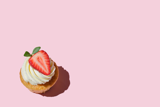 Fresh delicious sweet cake with strawberries and cream on a pink background, copy space for text, homemade cookies with strawberries and cream. White cupcake with big strawberry on top.