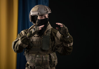 a male soldier in a military uniform and helmet on the background of the national flag of Ukraine