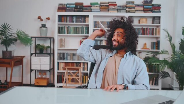 Young careless Arabian man amuses himself by launching airplane made of paper shirks from work and is lazy during absence of manager sits at table in office. Lack of professionalism concept