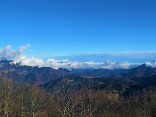 Scenic view of forest covered landscape of pre-alpine Slovenia with the peaks of the mountains in the Kamnik-Savinja alps out of the clouds on a clear blue day from Porezen in Gorenjska, Slovenia