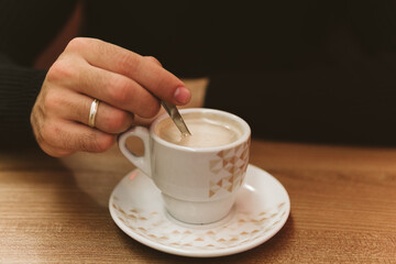 Hand of an unrecognizable young man with a cup of coffee in the foreground