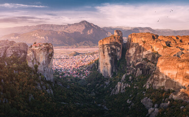 Fototapeta na wymiar Scenic panoramic view of the Monastery of the Holy Trinity in Meteora at sunrise and Kalambaka town at the distance. Tourist and pilgrimage experience. Natural and religious wonders of Greece.