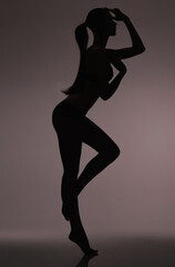 Fototapeta na wymiar Silhouetted beauty. Studio silhouette of a beautiful woman in lingerie against a gray background.