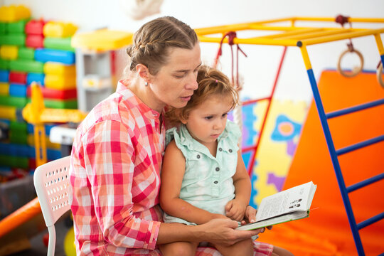 Teacher reads a book with a magical story to a little girl in kindergarten