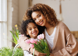 Grateful ethnic mother with bouquet hugging son