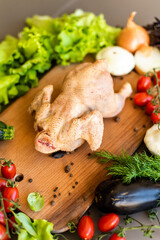 The chicken ready for cutting lies on a wooden board. Next to the chicken there are vegetables, peppers and lettuce. Recipe for cooking chicken with vegetables. Raw Chicken