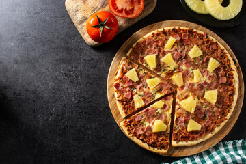 Hawaiian pizza with pineapple,ham and cheese on black stone. Copy space