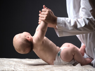 doctor lifts the hands of the baby lying on the table checking the reflexes of the newborn