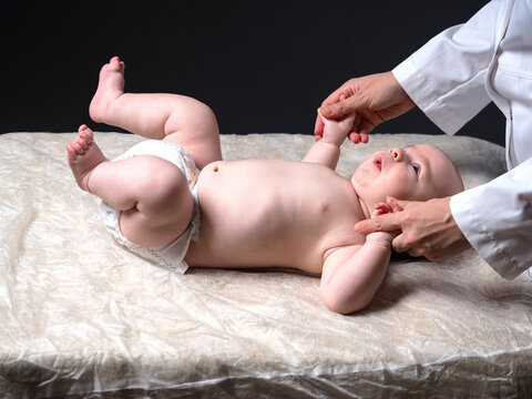 doctor lifts the hands of the baby lying on the table checking the reflexes of the newborn