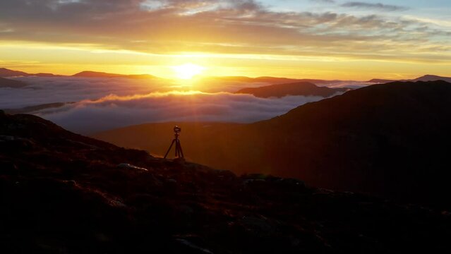 Mountain sunrise landscape with low clouds and a camera on a tripod making photography