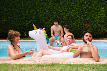 Group of people drinking lemonade and having fun in a swimming pool with a rainbow unicorn float.