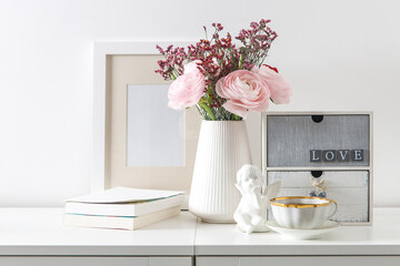 Bouquet of pink Persian buttercups on a white table in front of a chest of drawers. Scandinavian style. Place for text
