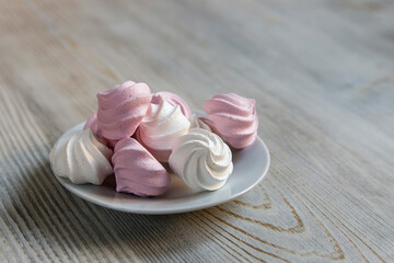 White and pink marshmallows on a white saucer on a beige table