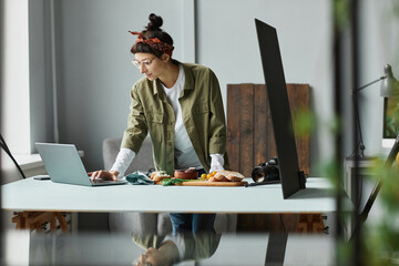 Side view portrait of female food photographer using laptop while setting up scene in studio, copy space