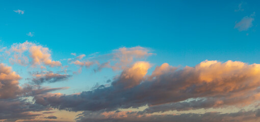 Panoramic view over deep blue sky with illuminated clouds at bloody sunset as a background.