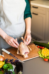 A girl is cutting up a chicken on a wooden plank. Next to it are some vegetables. The process of cooking chicken tobacco