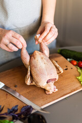 A girl is cutting up a chicken on a wooden plank. Next to it are some vegetables. The process of cooking chicken tobacco