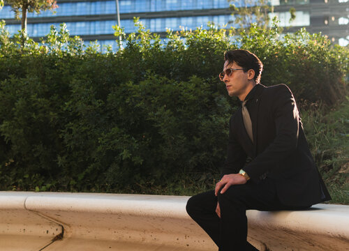 shot of a businessman wearing sunglasses sitting on bench of a park with his face looking at side who is about to raise up and leave