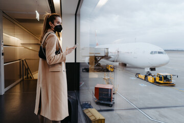 Young woman wearing a face mask and holding a mobile phone. Waiting at the airport 