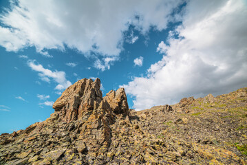 Scenic mountain landscape with stone outliers on rocky hill in sunlight under cloudy sky. Colorful scenery with sunlit sharp rocks on stone mountain under clouds in blue sky at changeable weather.