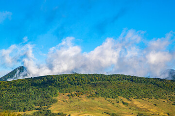 the hill is covered with trees and fields. blue sky with clouds. mountains landscape background.