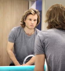 young man looking in the mirror,combing his hair,looking at problems on face.