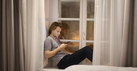 young man  sitting on the window sill,using smartphone