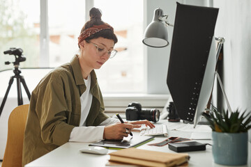 Side view portrait of female food photographer using computer while editing photos in studio, copy...