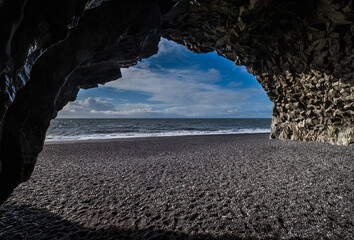 View to Reynisfjara ocean Black Sand Beach from cave at the foot of the Reynisfjall mount.Basalt rock pillars columns. Vik, South Iceland. Unique geological volcanic formations.