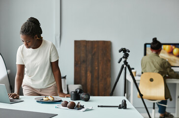 Portrait of young African American woman using laptop while working with food photography in...