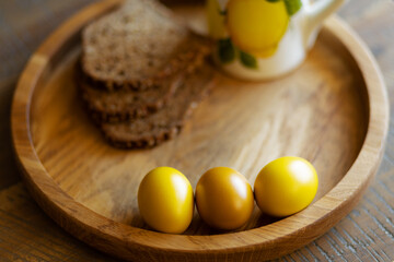 On a round wooden tray are three brightly colored Easter eggs and grain bread.