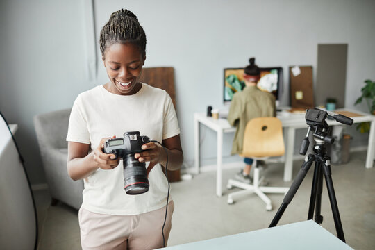 Portrait of smiling African American woman holding camera while working in photo studio, copy space