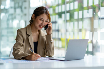 Portrait of a business woman using a laptop and talking on the phone with a customer. Happy working in the office