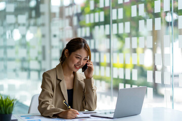 Fototapeta premium Portrait of a business woman using a laptop and talking on the phone with a customer. Happy working in the office