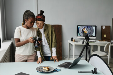 Portrait of two female photographers looking at photos in camera while working at photo studio,...