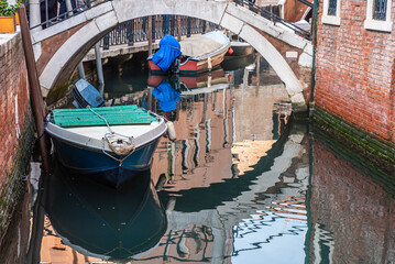 boat in a canal of venice with bridge and reflection in the water