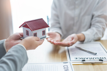 Insurance concept the estate agent holding a house model and giving it to his client