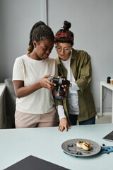 Vertical portrait of two female photographers looking at photos in camera while working at photo studio - obrazy, fototapety, plakaty