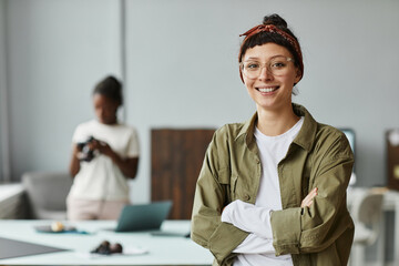 Waist up portrait of young female photographer smiling at camera while standing in photo studio,...