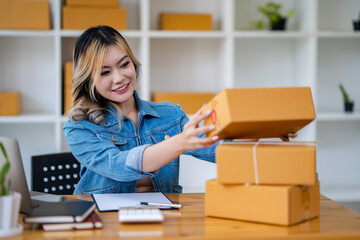 Obraz na płótnie Canvas Starting Small business entrepreneur SME freelance,Portrait young woman working at home office, BOX,smartphone,laptop, online, marketing, packaging, delivery, SME, e-commerce concept.